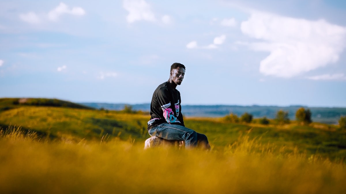 man in black jacket sitting on green grass field during daytime